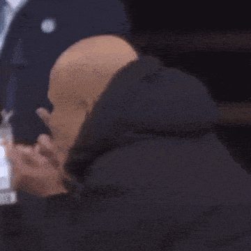 a bald man wearing a hooded jacket is covering his nose .