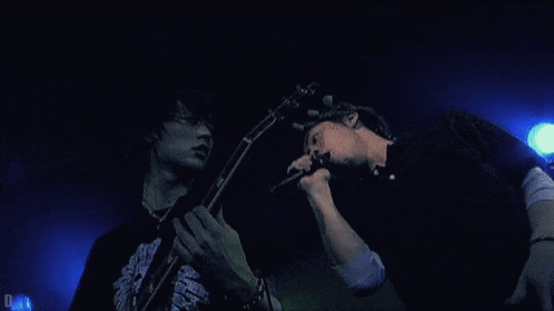 a man singing into a microphone while another man holds a guitar