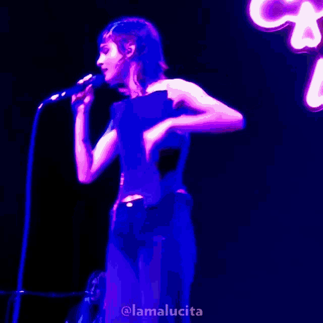 a woman singing into a microphone with the name lamalucita on the bottom left