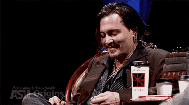 a man sitting at a table with a cup of coffee that says ash origins on it