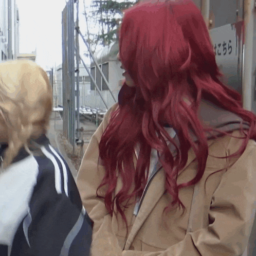 a woman with red hair stands in front of a sign that says こちら