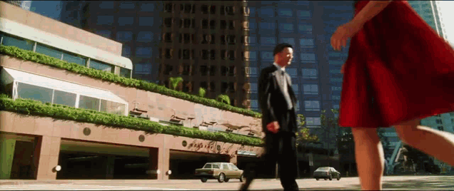 a woman in a red dress walks past a man in a suit and tie