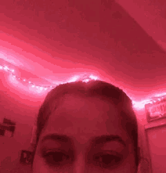 a close up of a woman 's face in a room with red lights hanging from the ceiling