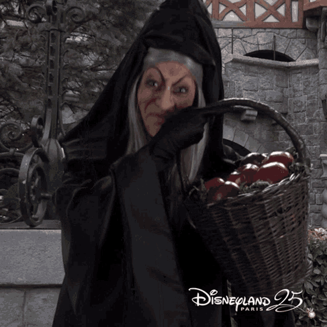 a woman in a witch costume is holding a basket of apples in front of a disneyland paris sign