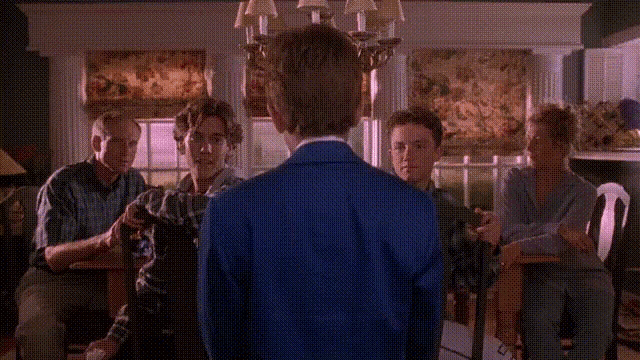 a boy wearing sunglasses and a blue suit is standing in a living room with other people .
