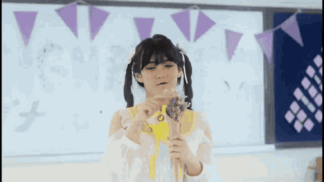a girl with pigtails is holding a bouquet of flowers in front of a white board with purple triangles on it
