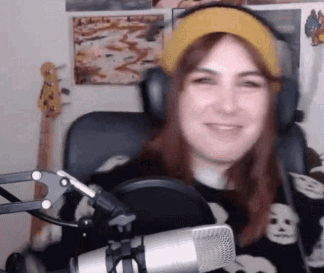 a woman wearing headphones and a hat is sitting in front of a microphone and smiling .