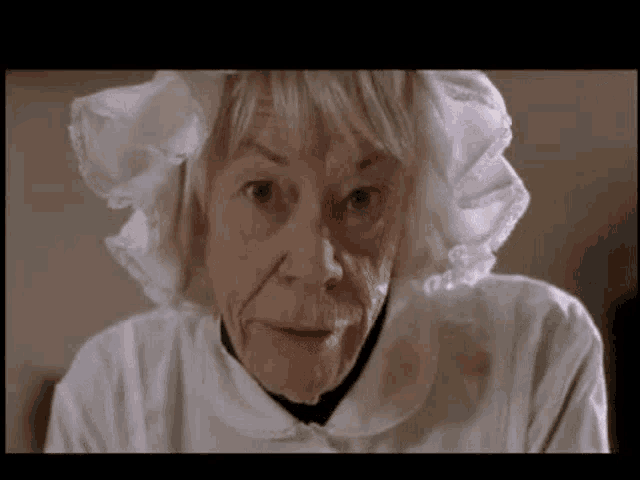 a close up of an elderly woman wearing a white dress and a white hat .