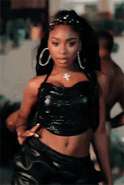a woman in a black crop top and leather shorts is standing in a room .