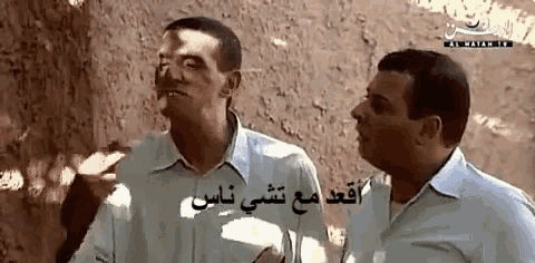 two men are standing next to each other in front of a wall with arabic writing on it ..