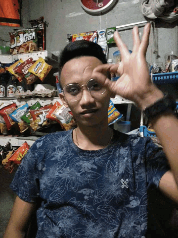 a man wearing glasses is making a funny face in front of a shelf of snacks including a bag of kettle corn