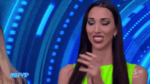a woman in a neon green dress applauds in front of a screen that says #gfvip