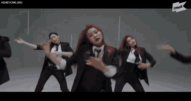 a group of women in suits and ties are dancing in front of a sign that says the k