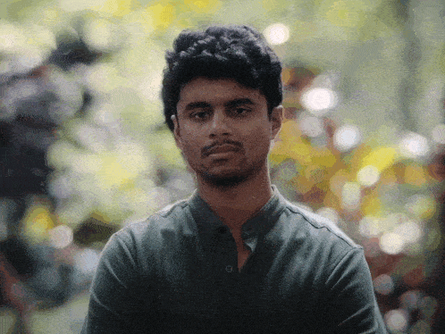 a man in a green shirt looks at the camera with trees in the background
