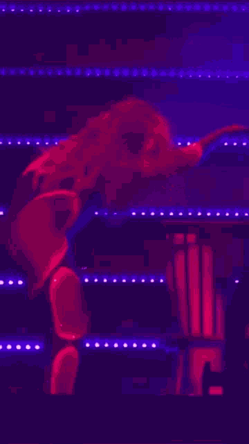 a woman in a red outfit is dancing in front of a row of purple lights