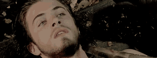 a man with a beard is laying on the ground with a knife in his mouth .