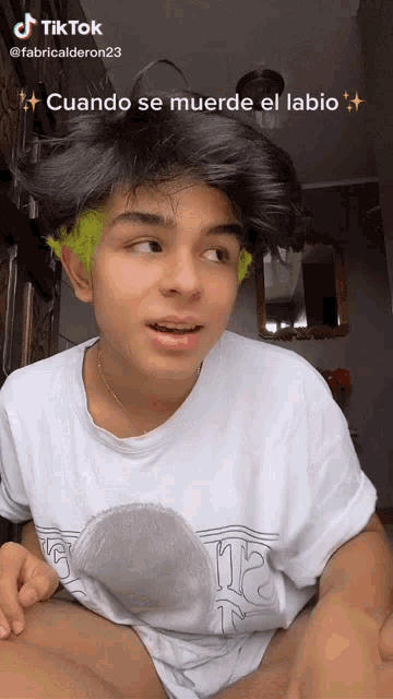 a young man with green hair is wearing a white t-shirt that says ' cuando se muerde el labio ' on it