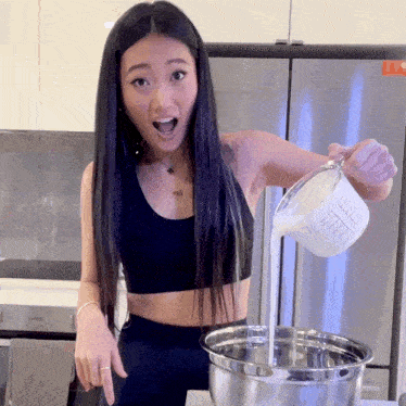 a woman is pouring liquid into a metal bowl with a measuring cup that says 1 cup