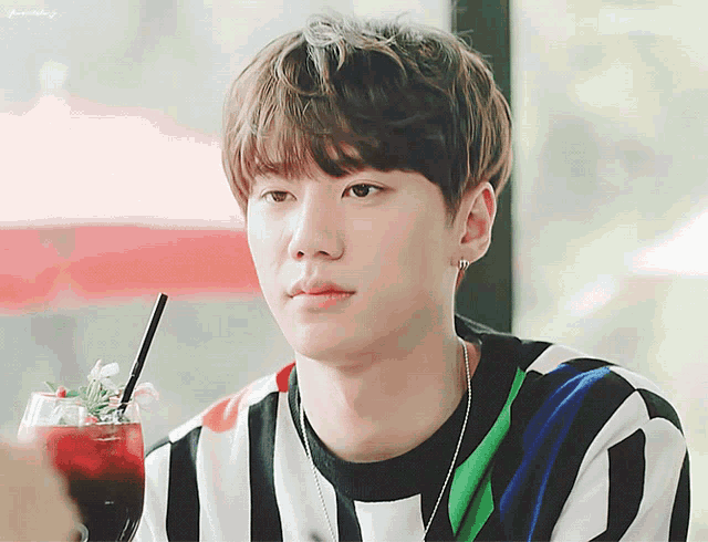 a young man in a striped shirt is holding a drink