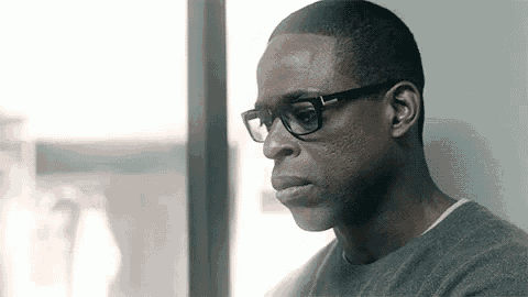 a man wearing glasses is leaning against a wall and looking out of a window .