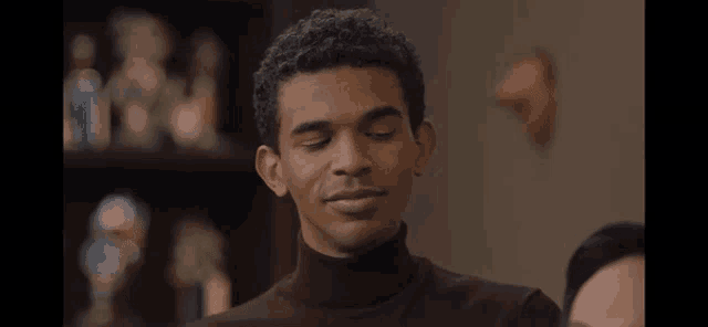a man in a brown turtleneck sweater is smiling in front of a shelf full of statues .