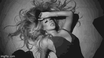 a black and white photo of a woman laying on the floor with her hand on her face .