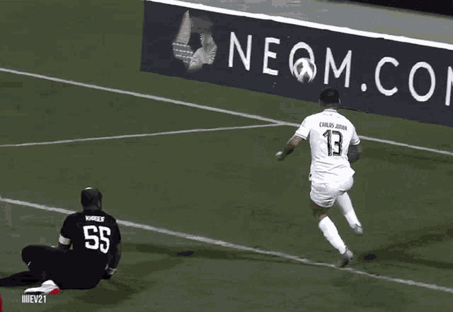 a soccer player is kicking a ball in front of a neon com sign