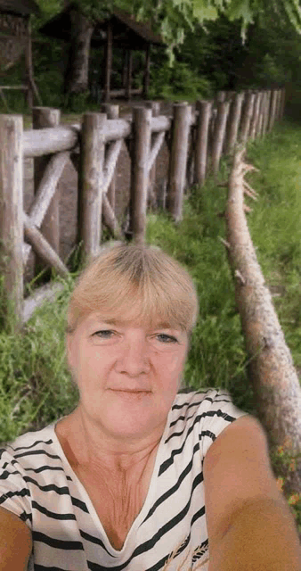 a woman in a striped shirt takes a selfie in front of a wooden fence