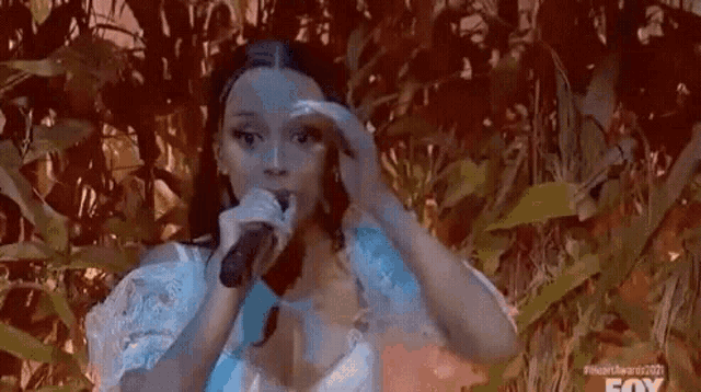 a woman is singing into a microphone while standing in a field of corn .