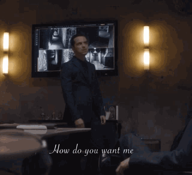 a man in a suit stands in front of a monitor and says how do you want me