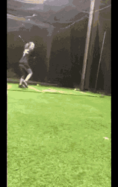 a woman is swinging a bat at a baseball on a green field .