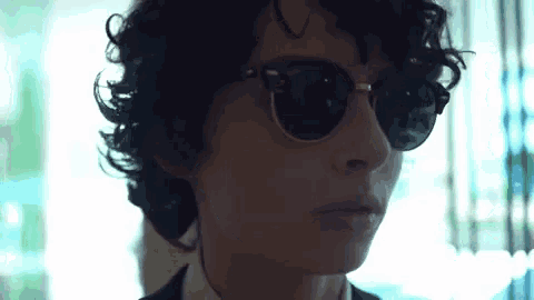 a young man wearing sunglasses and a suit is looking at the camera .
