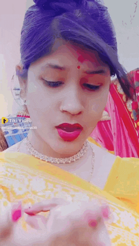 a woman wearing a yellow saree and a necklace is making a face .