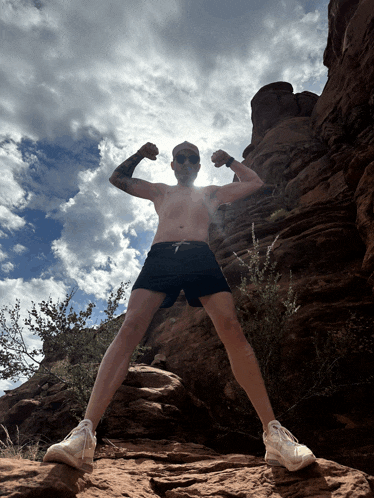 a shirtless man flexes his muscles while standing on a rock