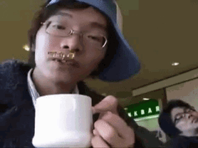 a man wearing glasses and a blue hat is holding a cup of coffee in his hand .
