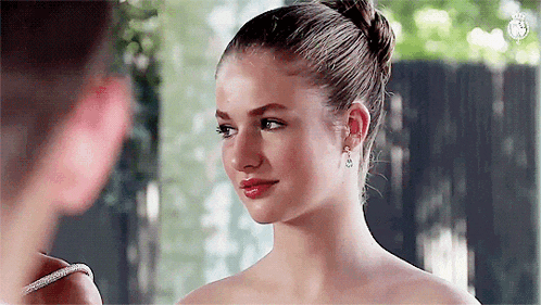 a woman in a white dress and earrings is looking at another woman in a mirror .