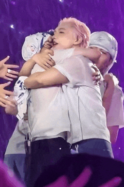 a group of people are hugging each other on a stage in front of a purple background .