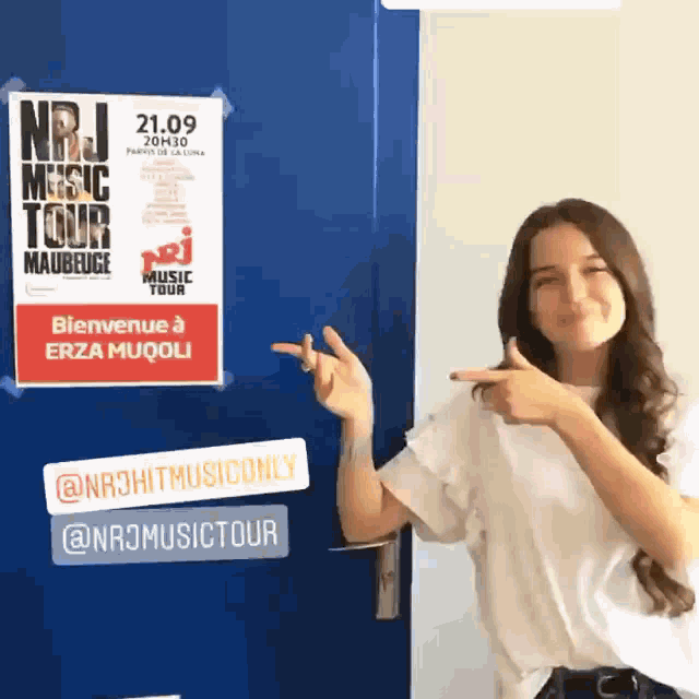 a woman standing in front of a door pointing at a sign that says nrj music tour maubeuge