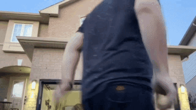 a man in a black shirt stands in front of a brick house