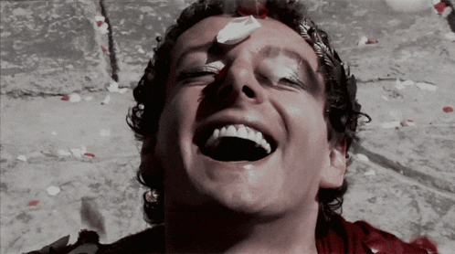 a man with blood on his face is laughing with petals falling around him