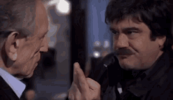 two men are talking to each other in a dark room and one of them is pointing at the other .