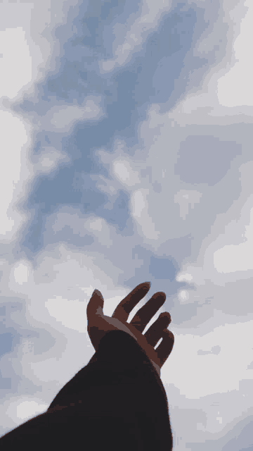 a person 's hand is reaching up into a cloudy blue sky