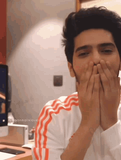 a man covering his mouth with his hands while wearing a white shirt with orange stripes