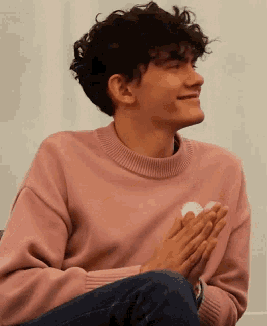 a young man with curly hair wearing a pink sweater with a heart on it