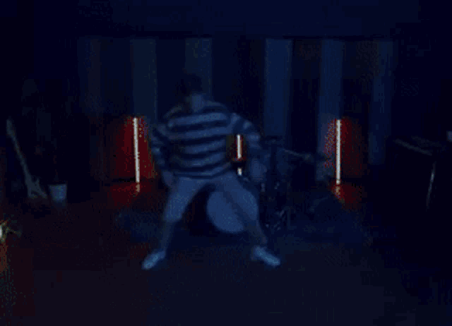 a man in a striped shirt is sitting on the floor playing drums .