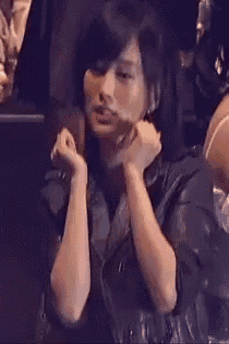 a woman is sitting in a dark room with her hands on her face and her mouth open .