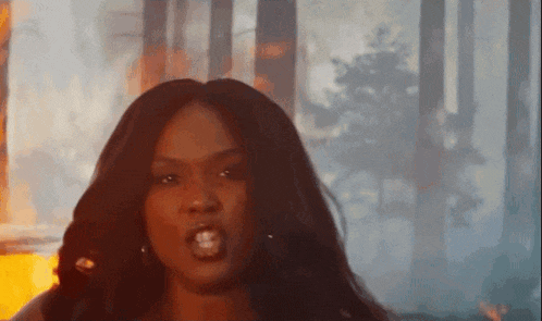 a woman with long hair is making a funny face in front of a forest fire .