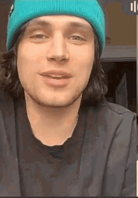 a young man wearing a blue beanie and a black shirt is smiling