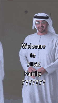 a man in a white robe is standing in front of a sign that says welcome to 7uae family 7777777