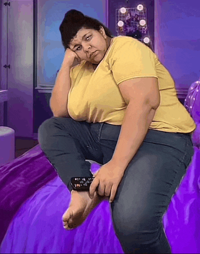 a woman in a yellow shirt is sitting on a bed holding a remote